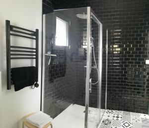 a glass shower in a bathroom with black tiles at Villa Moya, dependance privée Piscine & Spa in Châteauneuf-sur-Loire