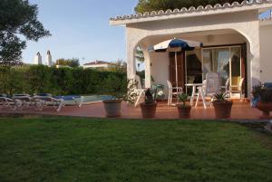 Cette maison dispose d'une terrasse avec des chaises et un parasol. dans l'établissement Villa Lombardi, à Alaior