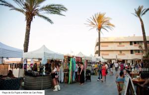 a group of people walking around a market with palm trees at Casa Can Relax in Es Pujols