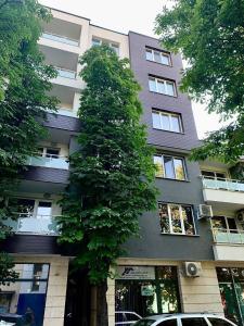 un edificio alto con un árbol delante de él en Comfort Deluxe Flat en Ruse