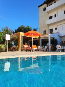 a woman sitting in a chair under an umbrella next to a swimming pool at Arhodiko Hotel in Amoudara Herakliou