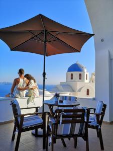 a man and a woman sitting on a table under an umbrella at Top Oia in Oia