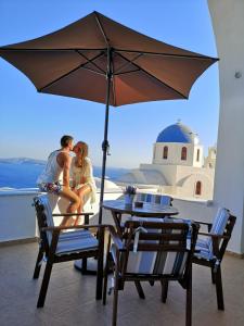a man and a woman sitting at a table under an umbrella at Top Oia in Oia