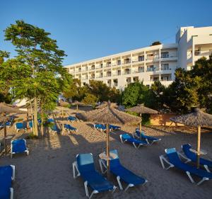 a beach with chairs and umbrellas and a building at Hotel Ses Savines in San Antonio