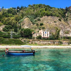 a boat in the water next to a beach at Taliari Taormina Apartment in Taormina