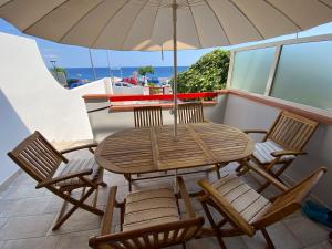 una mesa de madera y sillas con una sombrilla en el balcón en Casa Aletos Roccalumera-Taormina, en Roccalumera