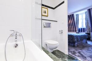 a bathroom with a tub and a toilet and a bed at Golden Tulip Washington Opera in Paris +27 photos