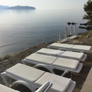 a row of white lounge chairs next to the water at Rosys Little Village in Skala