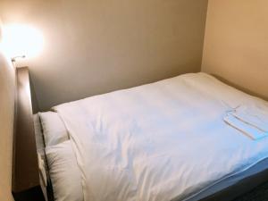 Cama blanca en habitación pequeña con luz en Business Hotel Sunpu, en Shizuoka