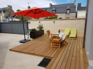 una terraza de madera con mesa y sombrilla roja en Appart 2 personnes proche plage de la Fresnaye, en Saint-Cast-le-Guildo