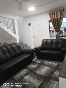 a living room with black leather couches and a staircase at Abah 2 Room Homestay in Pasir Gudang