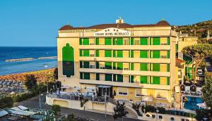 a large yellow building with green windows next to the ocean at Grand Hotel Michelacci in Gabicce Mare