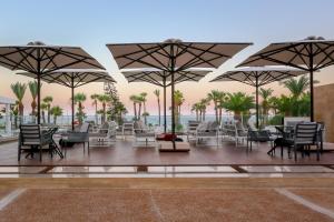 un patio con sillas, mesas y sombrillas en Golden Bay Beach Hotel en Lárnaca