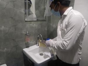 a man wearing a mask washing a bathroom sink at The Palm Tree -Family Stay in Amritsar