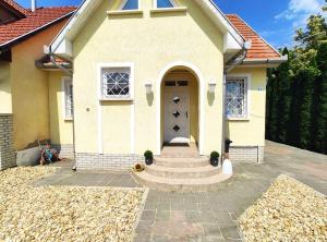 una pequeña casa amarilla con puerta y escaleras en Apollo Vendégház en Bogács
