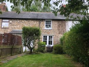una vieja casa de piedra con una valla y un patio en Mole Cottage en Stocksfield