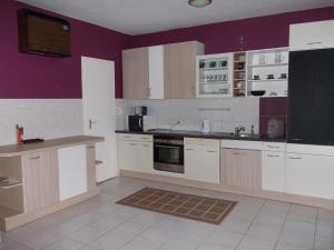 a kitchen with white cabinets and a purple wall at Aqua Apartman in Pécs
