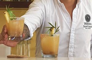 a person holding two cocktails on a counter at Merida Santiago Hotel Boutique in Mérida