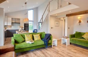 a living room with green couches and a kitchen at Hen Houses with Hot Tubs - Big Drift and Fairchilds Barn in Caldecott