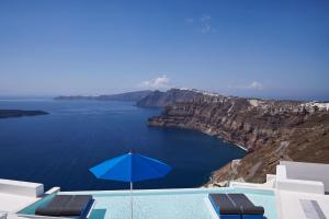 a swimming pool with a blue umbrella and chairs at Alti Santorini Suites - Caldera View in Megalokhori