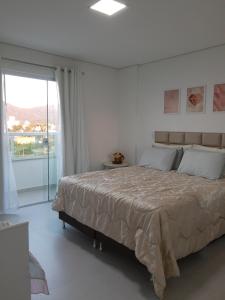 a white bedroom with a large bed and a window at Apartamento com vista pro mar próximo ao Beto Carrero in Penha