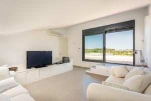 sala de estar con muebles blancos y TV de pantalla plana en Villa Canutells Ref 27, en Es Canutells