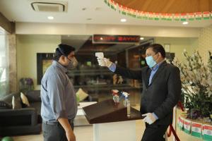 Un hombre con una máscara dándole a otro un celular. en Hotel Alleviate, en Agra