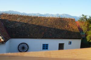 a white house with a rusty roof with mountains in the background at La Victorel in Porumbacu de Sus