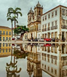 a reflection of a building and a palm tree in the water at Pousada Colonial Penedo - Alagoas in Penedo