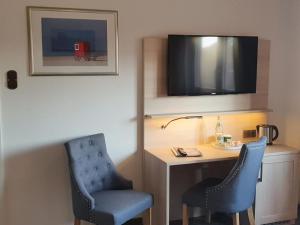 Zimmer mit 2 Stühlen, einem Schreibtisch und einem TV in der Unterkunft Hotel Pension Loose in Borkum