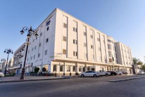 un grand bâtiment blanc avec des voitures garées devant lui dans l'établissement Mena Hotel Tabuk, à Tabuk