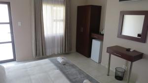 Un dormitorio con una cama, un escritorio y un espejo. en Villa Strada Guesthouse, en Klerksdorp