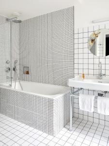 Baño de azulejos blancos con bañera y lavamanos en New Hotel Le Voltaire en París