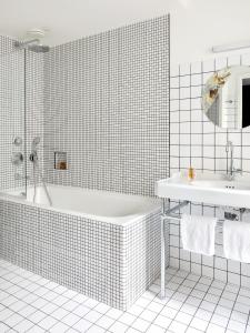 a white tiled bathroom with a tub and a sink at New Hotel Le Voltaire in Paris +37 photos