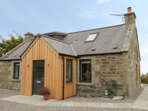 a wooden house in front of a stone building at Enzie Station Cottage in Buckie