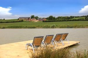 a group of chairs sitting on a dock on a lake at Hastings Retreat Rural barn conversions with Private Lake in Ashby de la Zouch