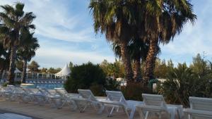 een rij witte stoelen op een patio met palmbomen bij Mobil home La Mer in Vias