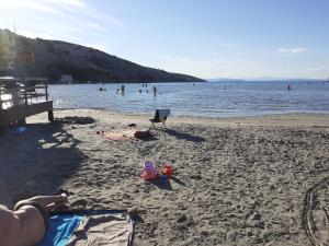 una persona sdraiata su una spiaggia con persone in acqua di Apartments Rajka a Lopar