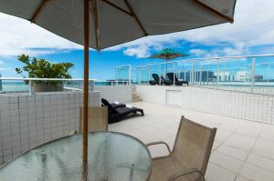 馬塞約的住宿－Slim Pajuçara by Tropicalis，阳台上的玻璃桌子和椅子,配有雨伞
