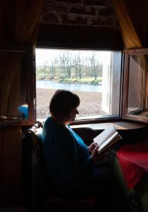 a woman sitting in a window reading a book at Baltā māja in Pilsrundāle