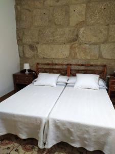 a bedroom with a white bed with a stone wall at A casa de Carmiña in Gondomar