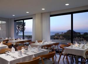 a restaurant with white tables and chairs and large windows at Cactus Hotel in Rhodes Town