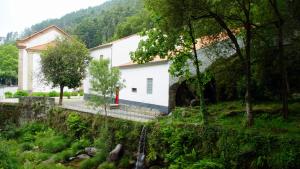 een wit gebouw met een rode deur naast een bos bij Casa Abrigo do Lagar in Amares