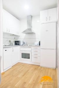 eine weiße Küche mit weißen Geräten und Holzböden in der Unterkunft Apartamento Caleta - FREE PARKING by Cadiz Time in Cádiz + 10 Fotos