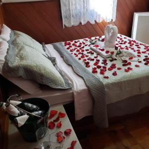 a bed with red roses on it with a table with a bunch of glasses at Pousada Recanto das Águas in Lumiar