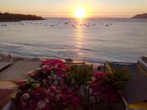 a sunset over the water with flowers and boats at Buganvilla Sea View apts in Agia Pelagia