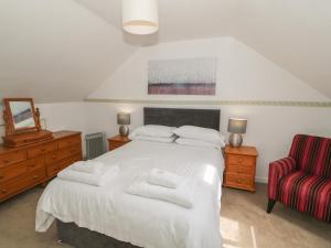 1 dormitorio con 1 cama blanca y 1 silla roja en 4 Ty Rhosyn, en Porthmadog
