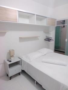 a white room with a bed and a night stand at Mar aberto suítes in Arraial do Cabo