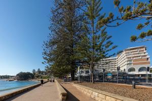 a person walking down a sidewalk next to the water at Crowne Plaza Terrigal Pacific, an IHG Hotel in Terrigal