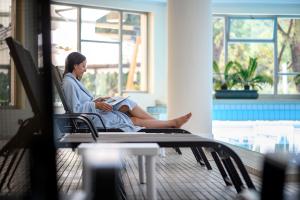 una mujer sentada en una silla leyendo un libro en Hotel Apollo Terme, en Montegrotto Terme